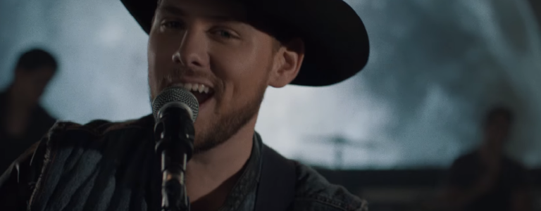 Brett Kissel singing while preforming on set with a moon in the background.